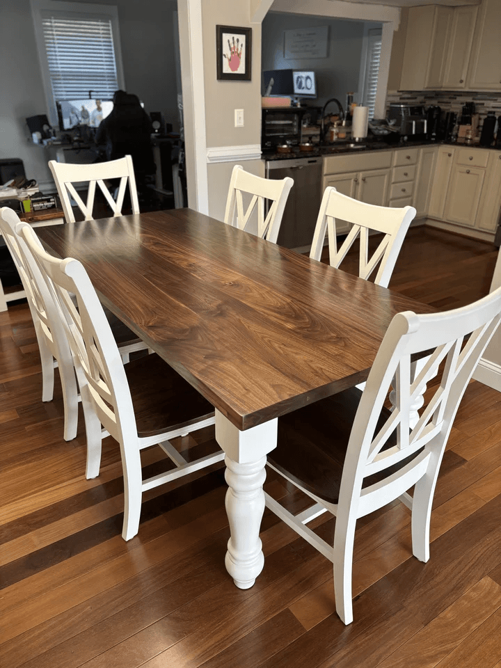 Large farmhouse dining table with dark stained wood top, white chunky turned legs, and white chairs in a home dining space.
